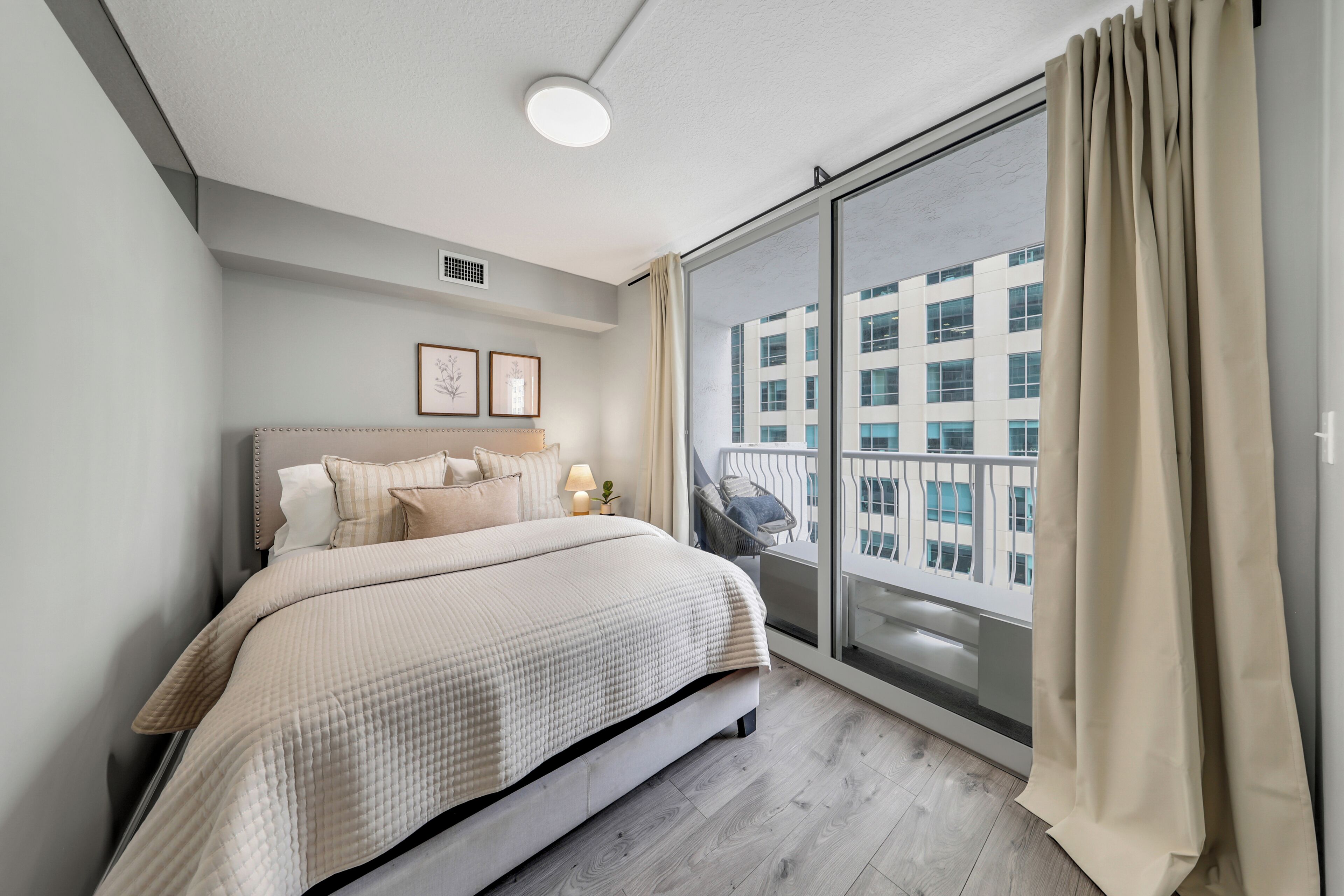A bedroom with a bed, a window with curtains, a wall-mounted light, and a framed picture.