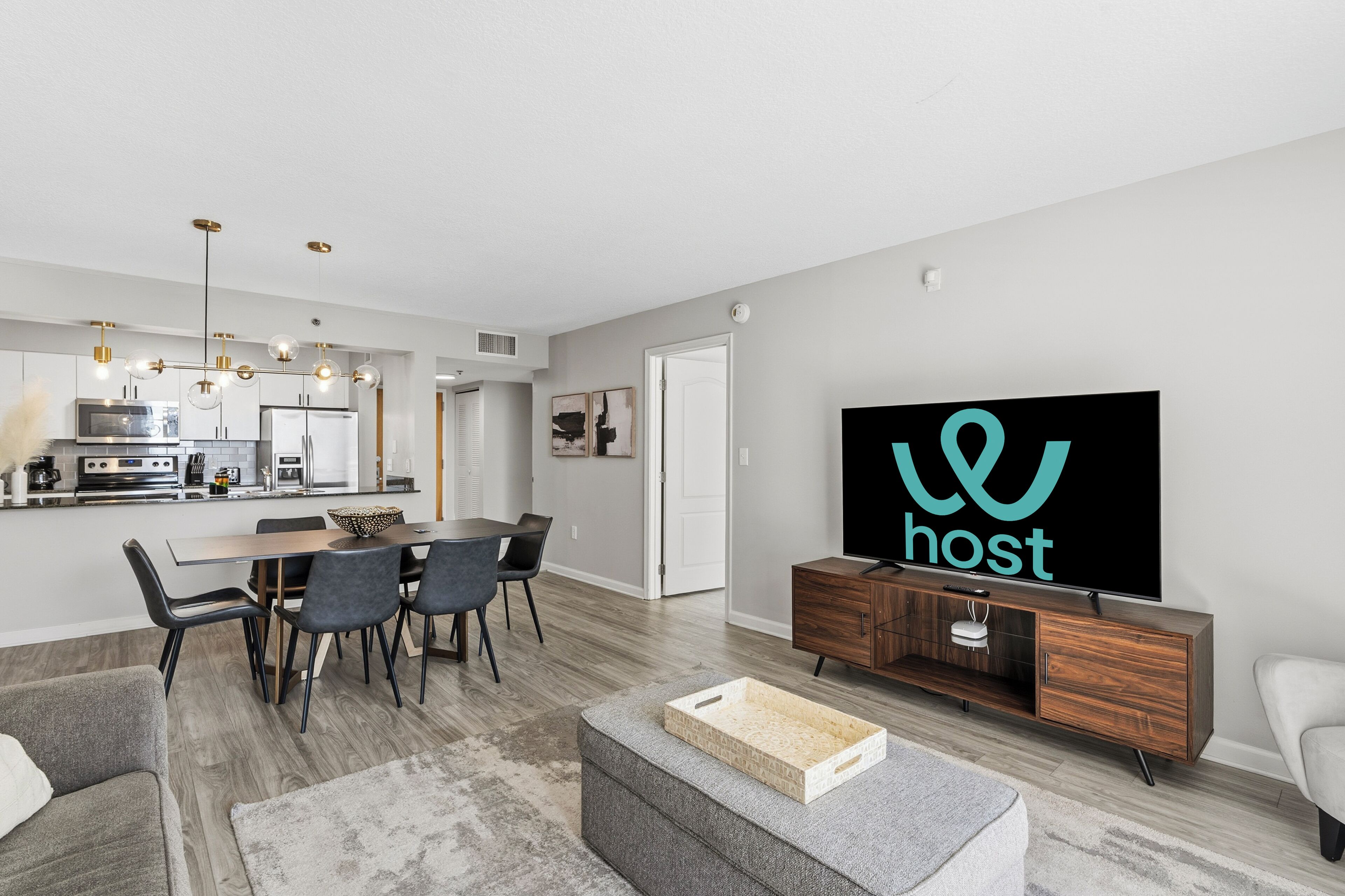 Uma sala de estar moderna com área de jantar, cozinha ao fundo e uma televisão grande exibindo a palavra 'host'.