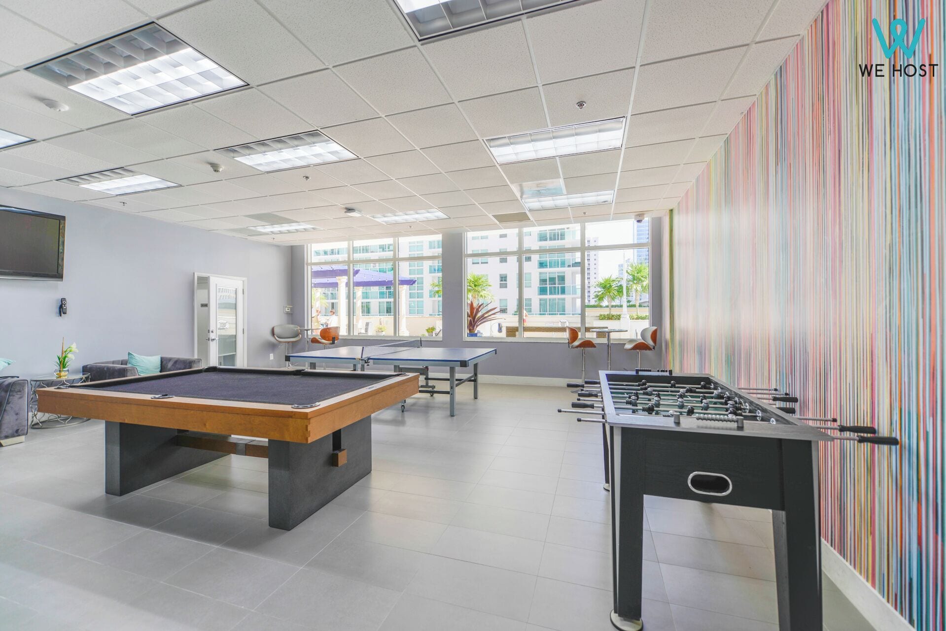 A modern indoor recreational area with a foosball table, ping pong table, and a pool table.