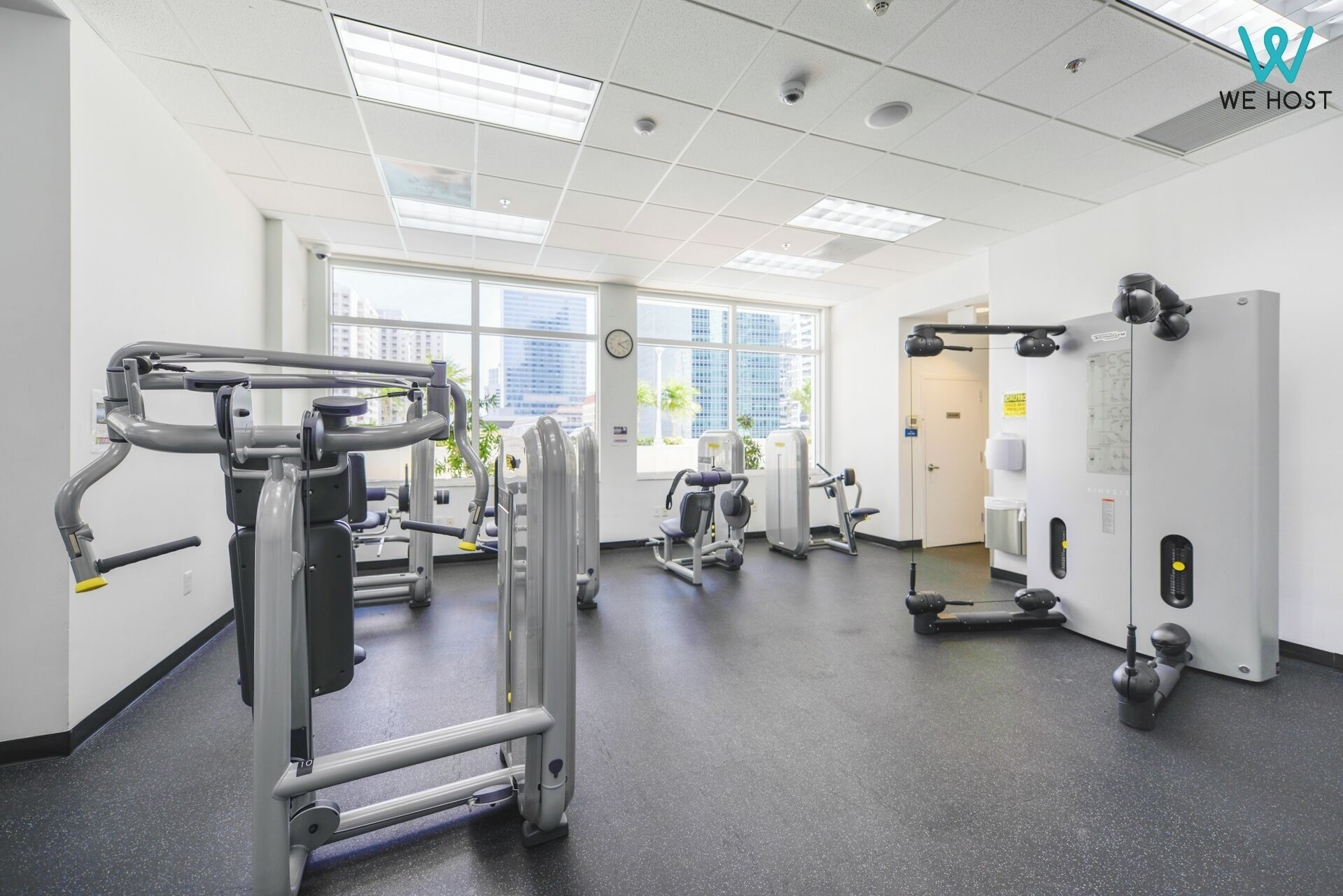A gym with various exercise machines, large windows, and a clean, modern design.