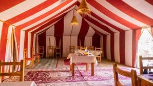 Una habitación con toldo, paredes a rayas, una mesa central con objetos y sillas de madera.