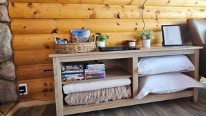 Un salon chaleureux avec un mur en bois, un téléviseur fixé au mur, une bibliothèque remplie de livres, une petite plante et un banc rembourré.