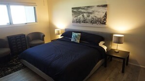 Une chambre à coucher avec un grand lit, deux lampes de chevet, une chaise, une commode et un tableau encadré au mur.
