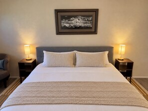 A neatly made bed with a gray headboard, two bedside lamps, and a framed picture on the wall.