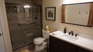 Une salle de bain avec une douche à parois de verre, des toilettes, un lavabo avec un miroir et un tableau encadré au mur.