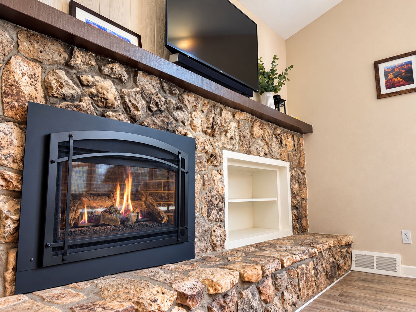 A stone fireplace with a TV above it, a shelf, and a framed picture on the wall.