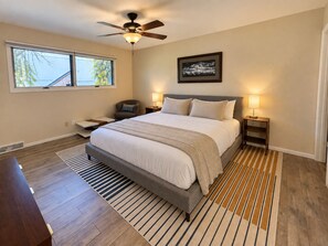 A bedroom with a bed, a ceiling fan, a window, a nightstand, and a rug.