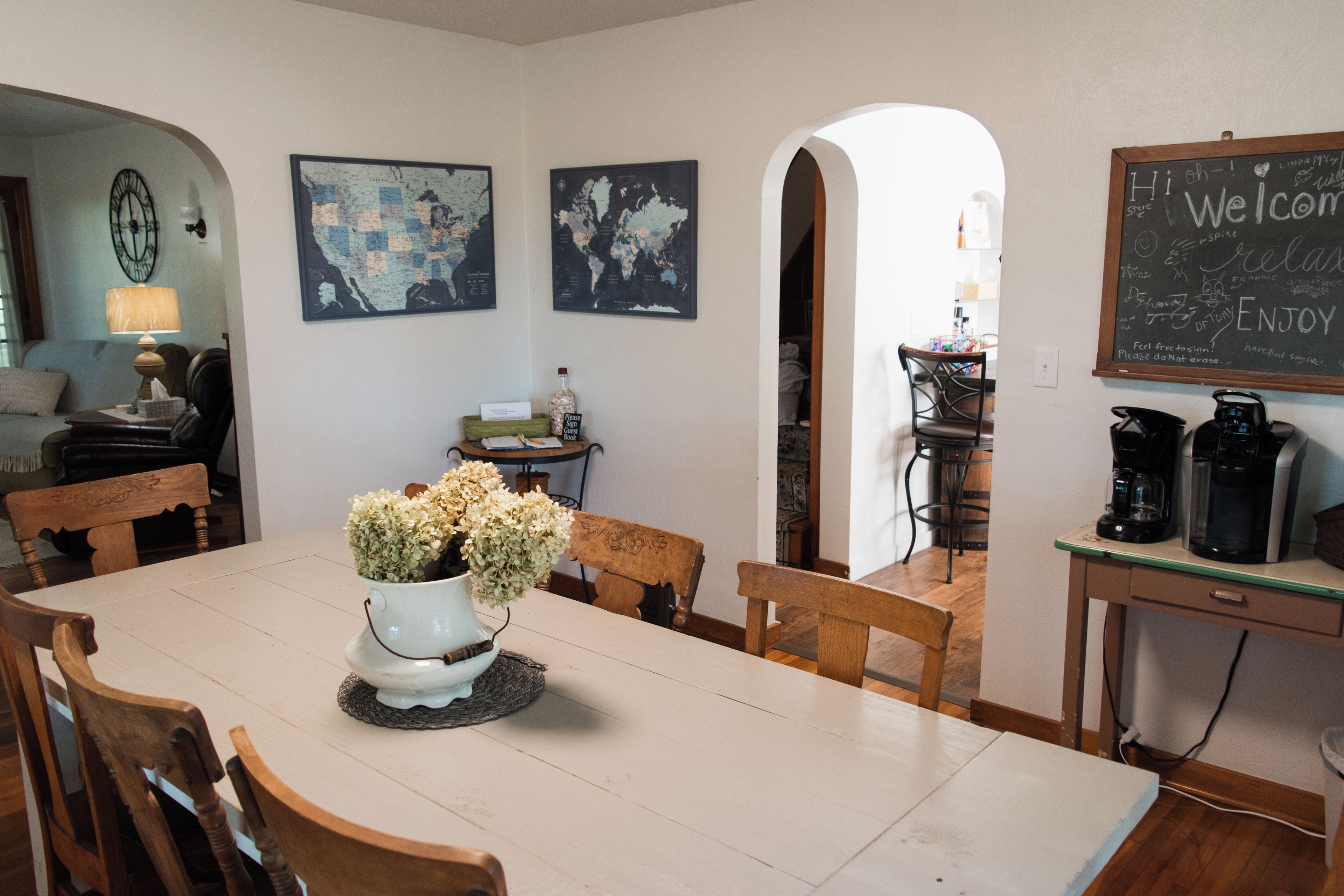 A dining area with a table, chairs, a vase of flowers, a wall with a world map, and a chalkboard with writing.