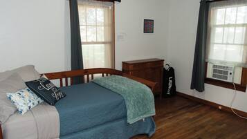 Een slaapkamer met een bed, een dressoir, een raam met gordijnen en een wandairconditioner.