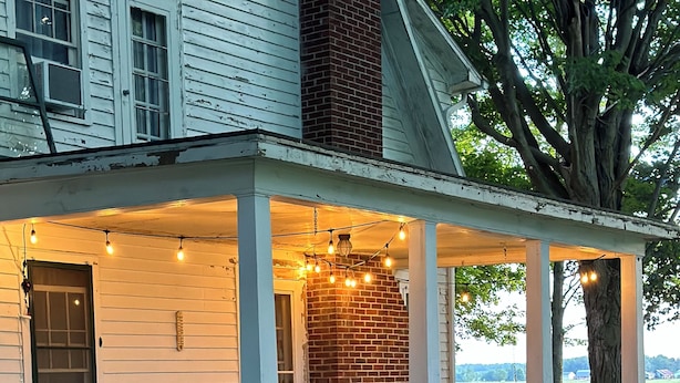 A covered porch with two chairs and a table, a brick wall, and string lights.