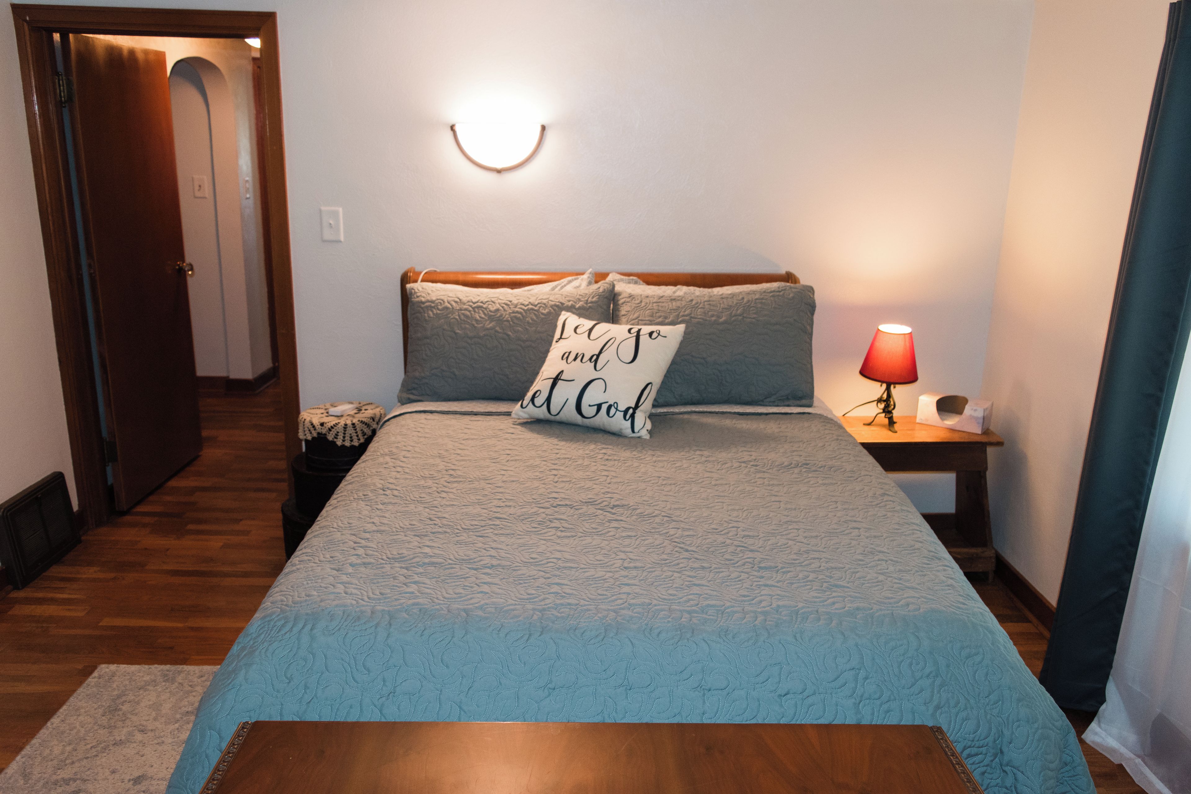 Une chambre à coucher comprenant un lit, une lampe de chevet, une table de chevet et une porte donnant sur une autre pièce.