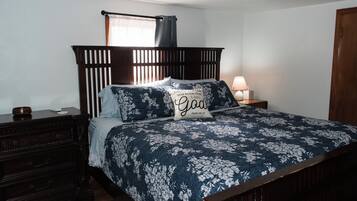 Una camera da letto con una testiera in legno, un letto con biancheria a fiori, una lampada da comodino e un comodino con una ciotola.