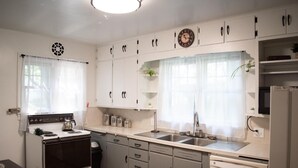 A compact kitchen with a stove, sink, and dishwasher, featuring white cabinets and a clock on the wall.