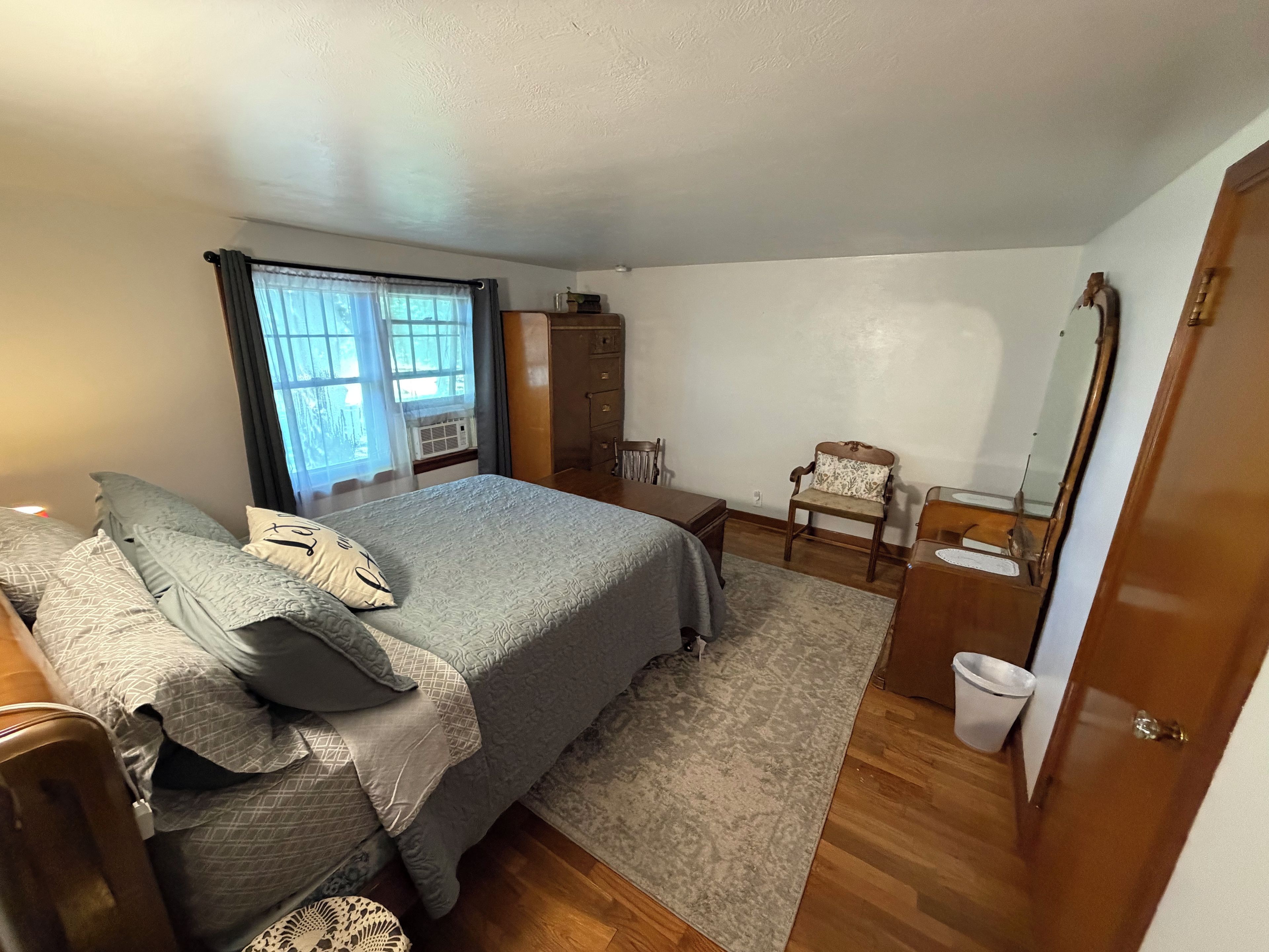 A bedroom with a bed, bedside table, dresser, chair, and a mirror.