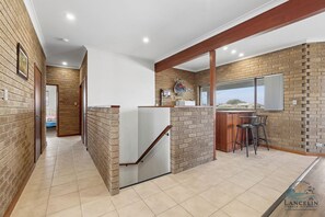 A kitchen with brick walls, a wooden beam ceiling, a bar area with stools, and a view through a window.
