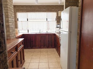 A kitchen with wooden cabinets, a white refrigerator, and a window with lace curtains.