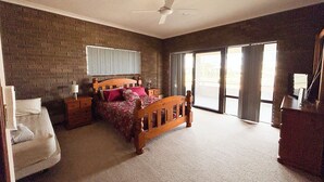 A bedroom with a brick wall, a bed with a wooden headboard, a nightstand, a dresser, and a sliding glass door leading to an outdoor area. - Sandcastle: 6x2 home with stunning views of both the ocean and the sand dunes  (Lancelin)