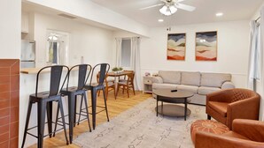 Ein geräumiger Wohnbereich mit Sofa, Couchtisch und Sesseln, ein Essbereich mit Tisch und Stühlen sowie eine Küche mit Kühlschrank und Schränken.
