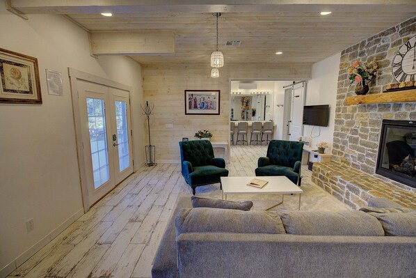 A living room with a stone fireplace, two green armchairs, a white coffee table, and a television mounted on the wall. - Shay Meadows Ranch & Resort #2500 (Big Bear City)