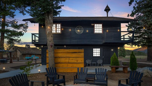 Un bâtiment de style rustique, semblable à un chalet, doté d’un foyer, de sièges extérieurs et de guirlandes lumineuses.