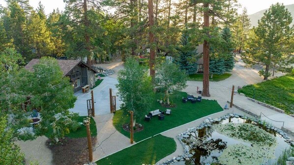 Un chalet entouré de grands arbres, avec une pelouse bien entretenue et un petit étang.