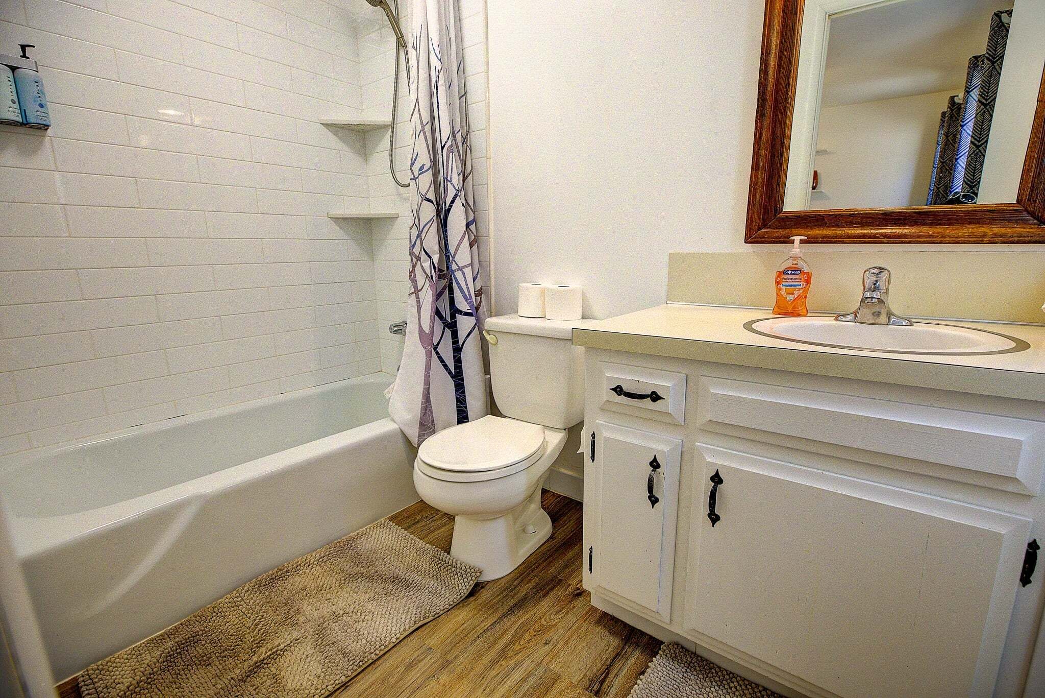 A bathroom with a white bathtub, toilet, and vanity with a mirror.