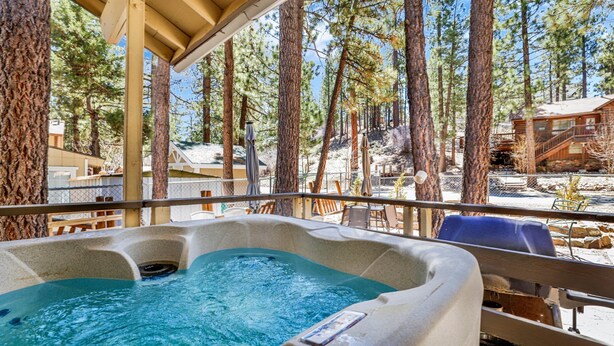 A hot tub with a wooden deck and a view of a forested area. - Reality Escape #2466 (Big Bear City)