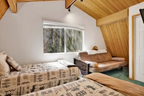 A cozy room with two beds, a window with a view of trees, and a wooden ceiling. - OUR Cabin IN THE Woods #2476 (Big Bear Lake)