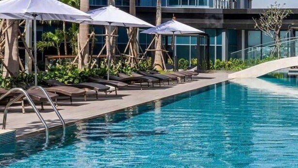 A swimming pool with lounge chairs and umbrellas, a glass bridge, and modern architecture. - DongDong Apartment in Sunwah Pearl (Ho Chi Minh City)