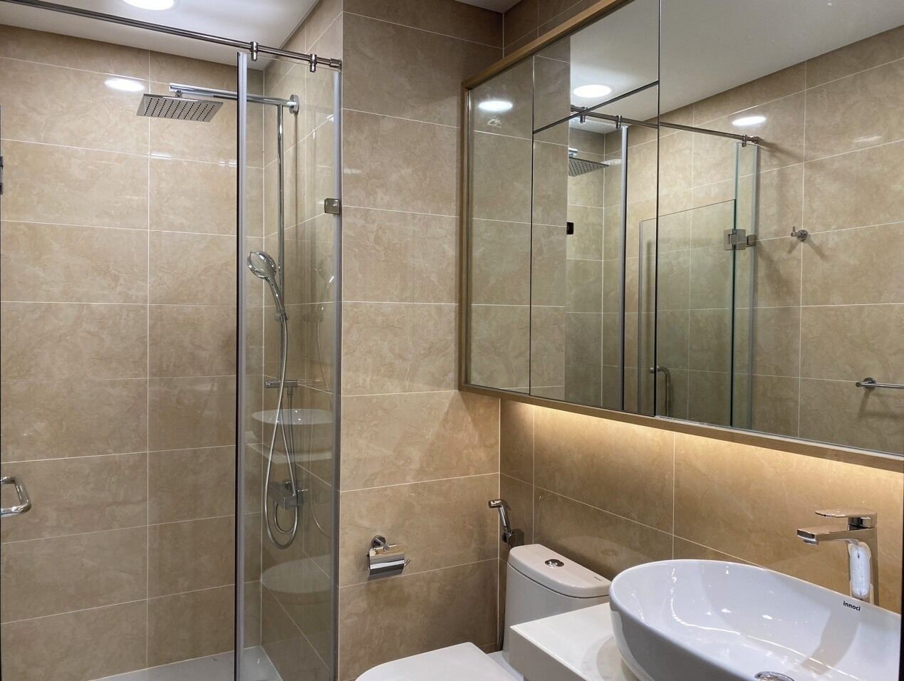 A modern bathroom with a glass-enclosed shower, a white sink, and a large mirror.