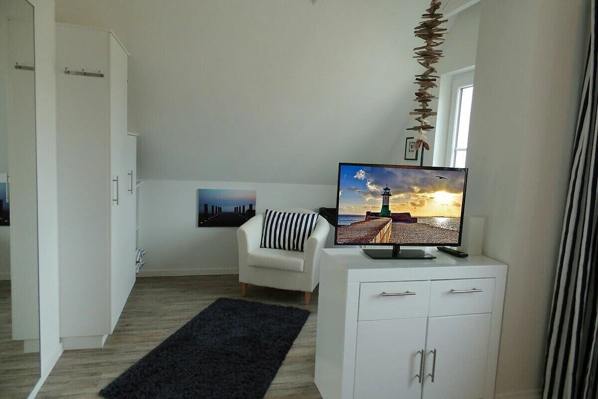 A modern living room with a flat-screen TV, a white sofa, a black rug, and a white cabinet.