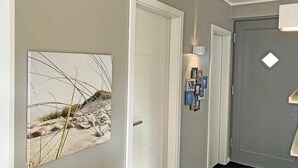 Un couloir avec un tableau encadré représentant une scène de plage, une porte blanche et un luminaire fixé au mur.