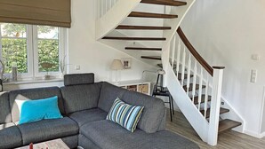 Un salon moderne avec un canapé d’angle gris, une table basse en bois et un escalier doté de rampes blanches.