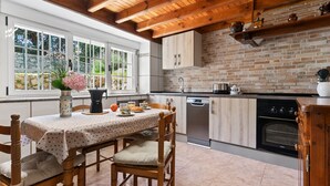 Une cuisine avec des poutres en bois, un mur en briques, une table à manger avec des chaises et une vue sur la verdure à l’extérieur.