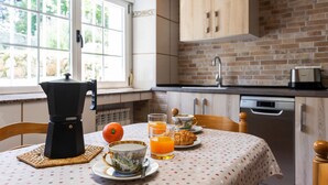 Une cuisine avec une machine à café, des oranges, des verres de jus d’orange et une nappe à pois.