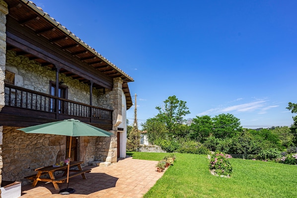 A stone building with a wooden balcony, a picnic table, and an umbrella.