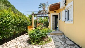 Une cour avec un chemin en pierre, une pergola et un bâtiment doté d’une porte et d’une fenêtre.