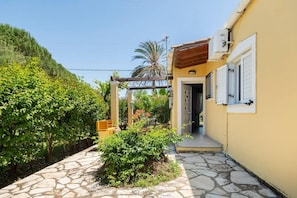 A courtyard with a stone pathway, a pergola, and a building with a door and window. - Apartment 'Iris One-Bedroom Bungalow' with Shared Pool, Wi-Fi and Air Conditioning (Corfu)