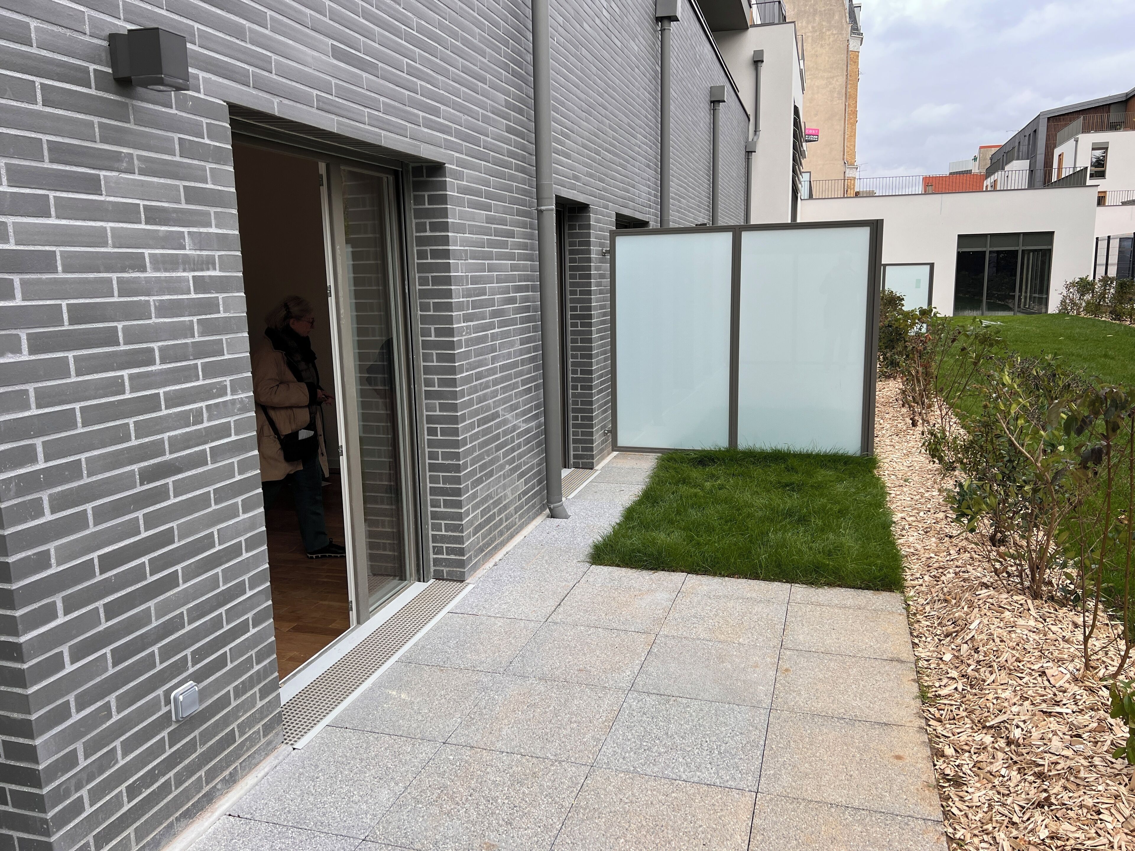 Un bâtiment moderne avec une façade en briques, une entrée dotée d’une porte en verre et un petit espace verdoyant recouvert de paillis.