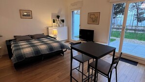 A bedroom with a bed, a desk, and chairs. There is a window with a view of the outdoors.