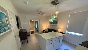 Une cuisine moderne avec un îlot central, un coin repas avec une table et des chaises, et un salon avec un canapé et un téléviseur.