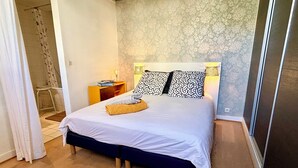 Quarto com cama, mesa de cabeceira, luminária e área de chuveiro.