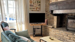 Ein gemütliches Wohnzimmer mit Kamin aus Naturstein, einer bequemen Couch und einem Flachbildfernseher auf einem Lowboard.