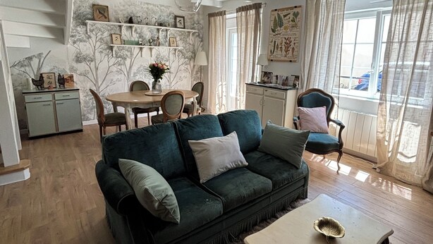 Ein Wohnzimmer mit einem dunkelgrünen Sofa, einem Couchtisch und einem Essbereich mit Tisch und Stühlen.