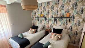 Ein Zimmer mit zwei Betten, einer hängenden Lampe, einem gemusterten Wandpapier und einem Holzboden.