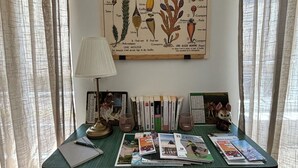 Ein Arbeitszimmer mit einer botanischen Illustration, Büchern und einer Lampe.