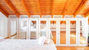 Ein Schlafzimmer mit Holzbalkendecke, einem Bett und einem Kleiderschrank mit Spiegelüren.