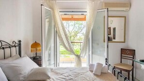 Une chambre à coucher comprenant un lit, une chaise, une table de chevet, une lampe, une fenêtre avec des rideaux et un appareil de climatisation.