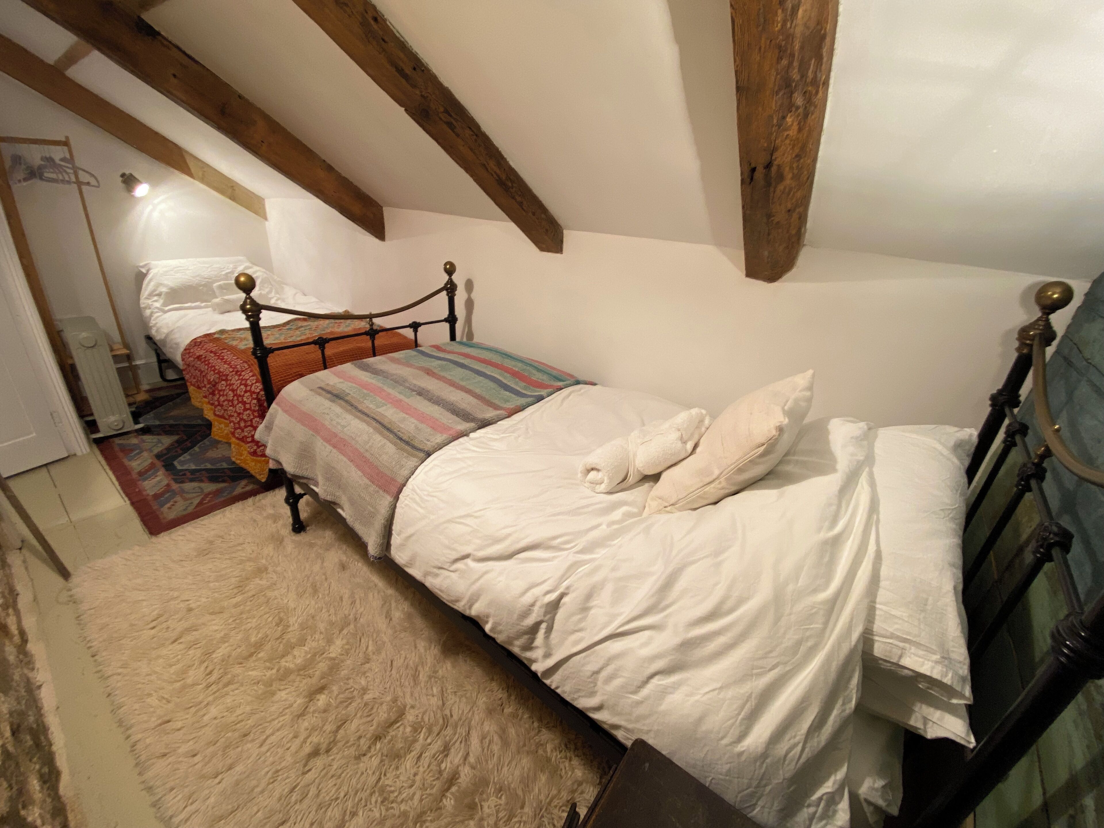 Een slaapkamer met een bed, een pluizig vloerkleed en zichtbare houten balken.