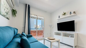 Una sala moderna con un sofá color turquesa, un televisor de pantalla plana, una consola blanca y un ventanal corredero que da a un espacio al aire libre.